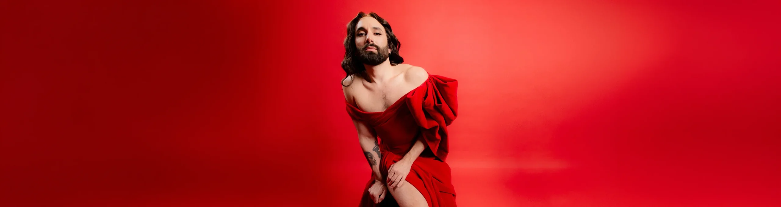 Conchita Wurst in rotem Kleid vor rotem Hintergrund