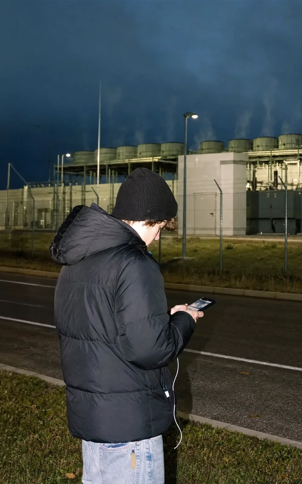 Eine junge Person betrachtet ihr Smartphone vor einem großen Rechenzentrum bei Wien.