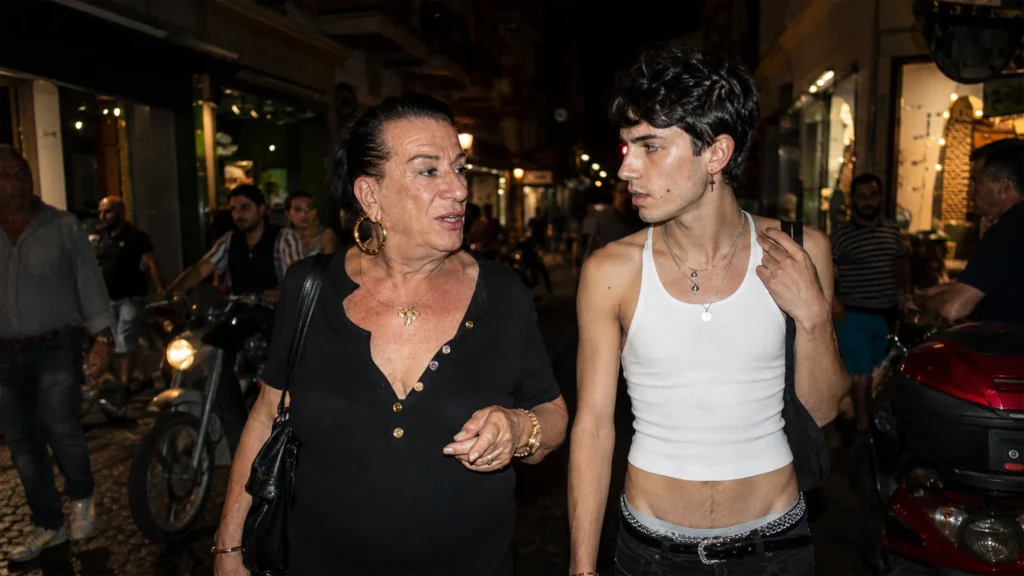 Ein älterer Femminiello und eine jüngere queere Person stehen gemeinsam auf einer Straße in Neapel.