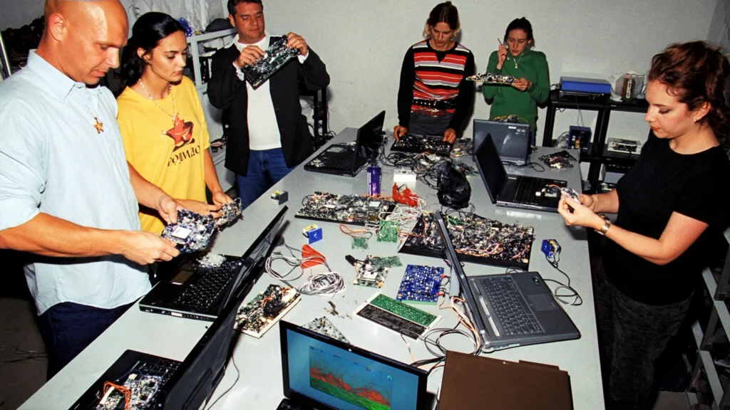 Mehrere Menschen reparieren alte Computer und Netzwerkgeräte in einer Wiener Gemeinschaftswerkstatt.