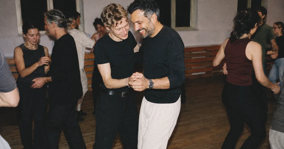 Zwei erwachsene Männer unterschiedlichen Alters lernen gemeinsam neue Bewegungen in einem Wiener Tanzworkshop.