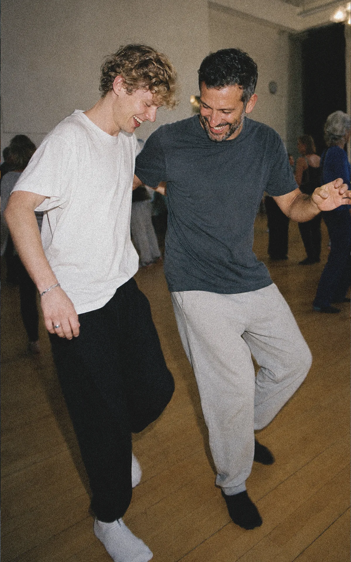 Zwei erwachsene Männer unterschiedlichen Alters lernen gemeinsam neue Bewegungen in einem Wiener Tanzworkshop.