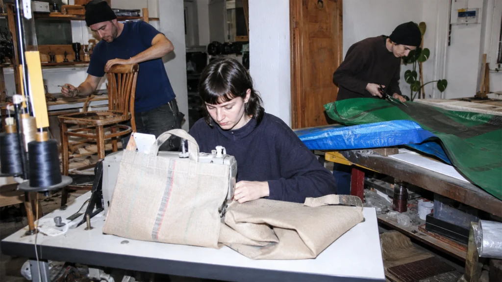 Mehrere Menschen verarbeiten gebrauchte Säcke, Planen und Möbel in einer Wiener Upcycling-Werkstatt.