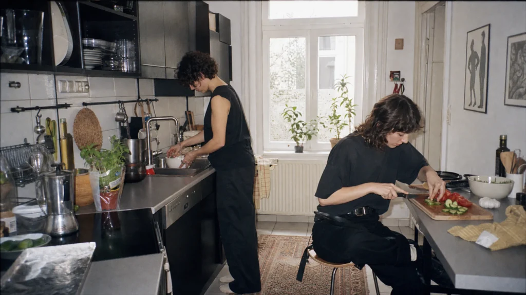 Zwei Erwachsene bereiten in einer barrierefreien Wiener Küche gemeinsam eine Mahlzeit zu, eine Person arbeitet im Sitzen.