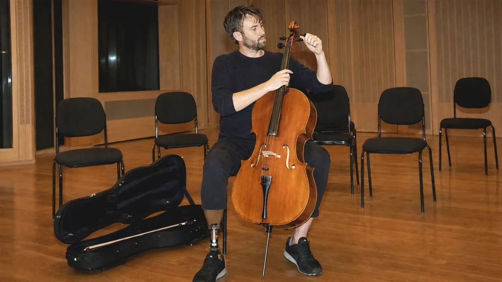 Eine Person mit Unterschenkelprothese stimmt in einem Wiener Proberaum ein Cello.