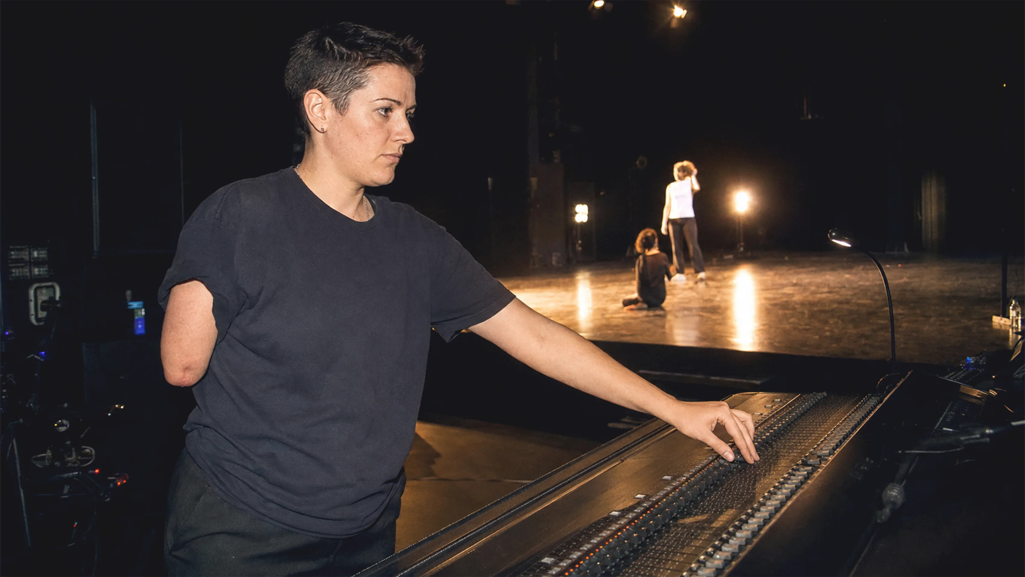 Eine Person mit einer Oberarmdifferenz leitet an einem Lichtpult eine Theaterprobe in Wien.