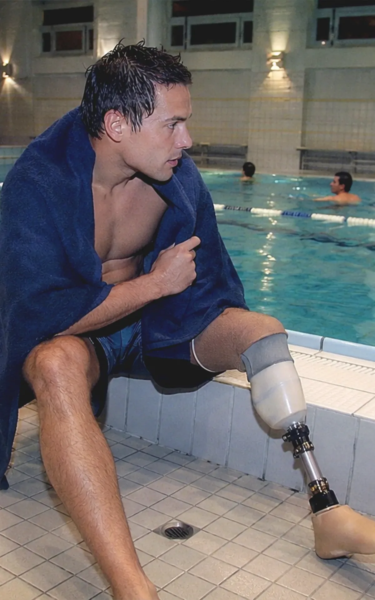 Ein junger Mann mit Beinprothese sitzt nach dem Schwimmen an einem barrierefreien Wiener Hallenbad und blickt ruhig auf das Wasser.