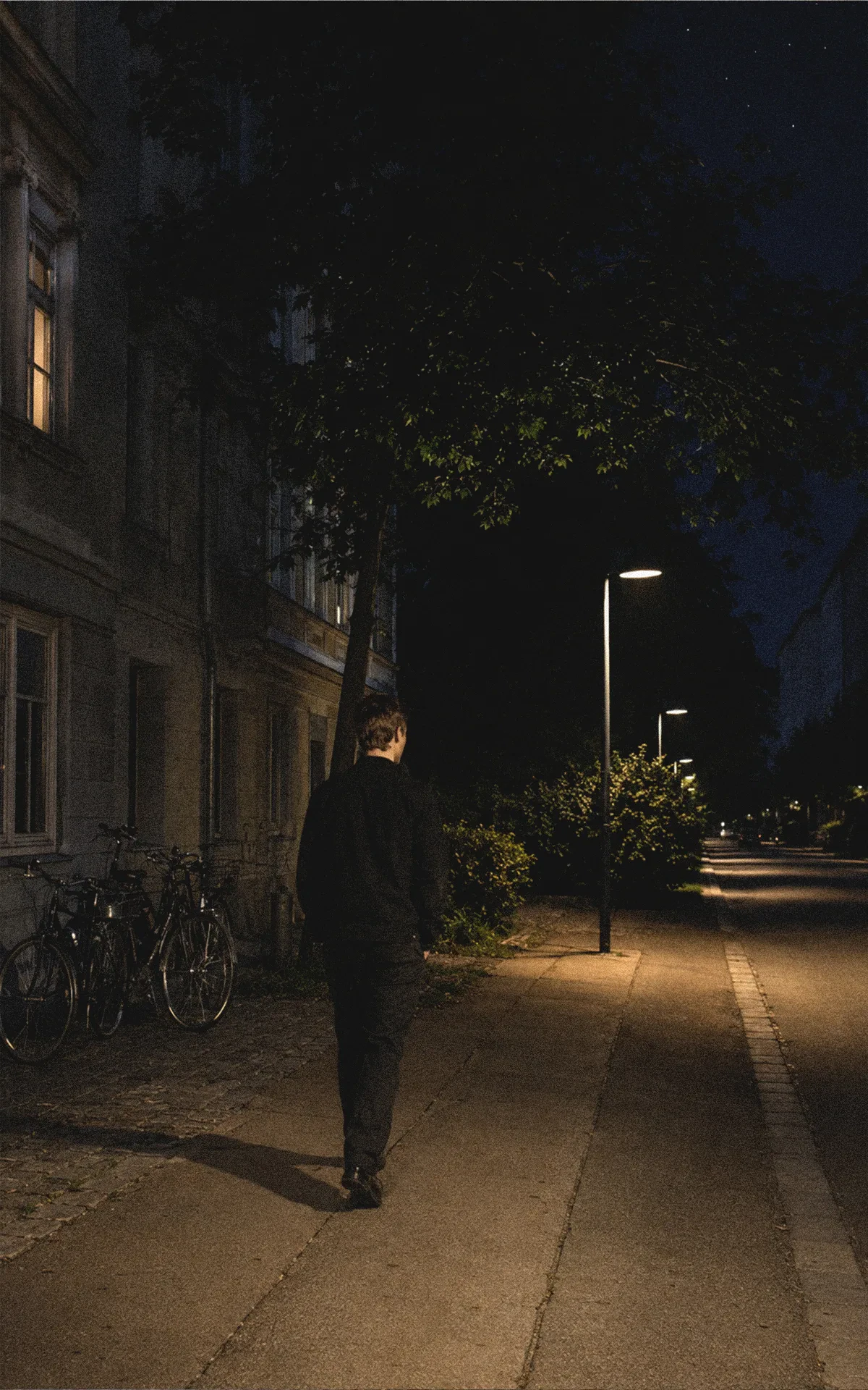 Junger Mann geht nachts unter abgeschirmten Straßenleuchten durch eine ruhige Wiener Straße