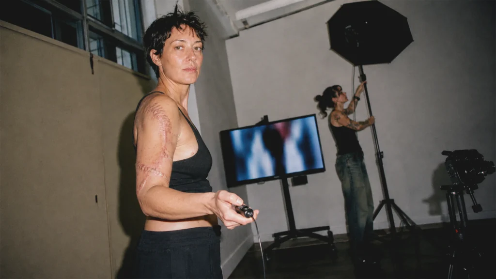 Eine erwachsene Person mit sichtbaren Operationsnarben steuert in einem Wiener Fotostudio selbst die Aufnahme eines Porträts.