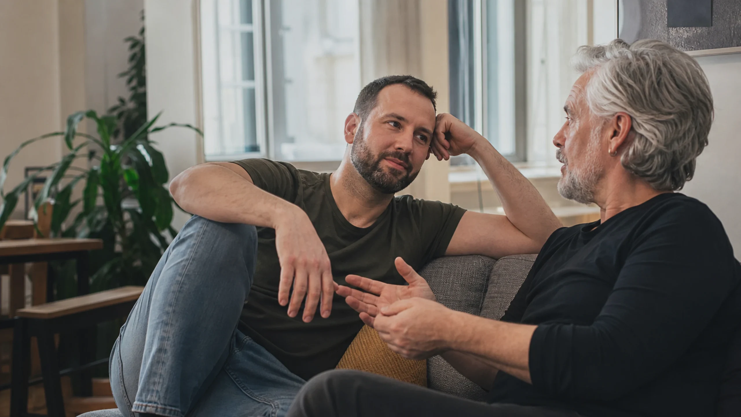 Zwei schwule Männer unterschiedlicher Generationen sprechen in einem ruhigen Innenraum über das Älterwerden.