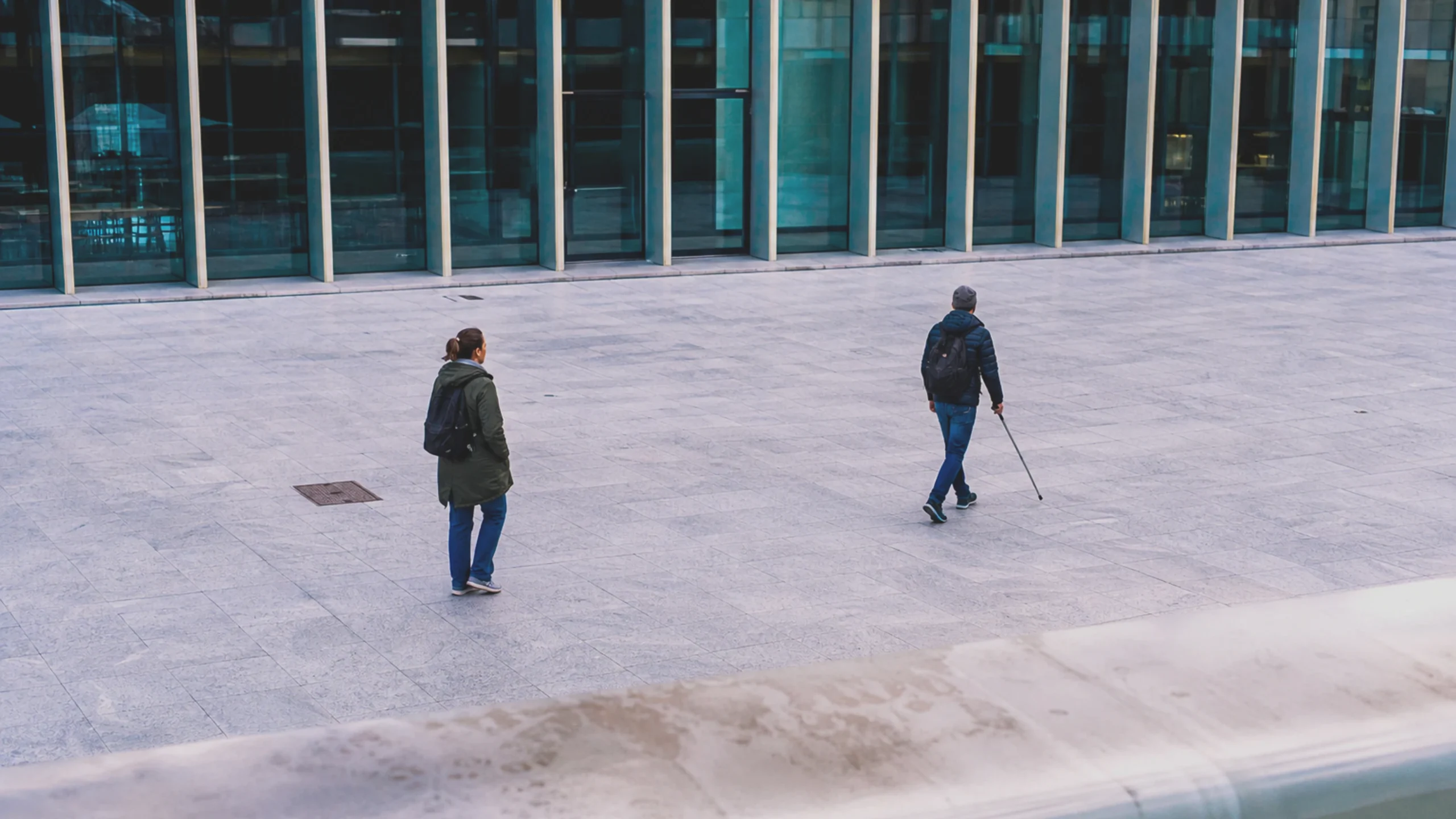 Un adulte handicapé traverse de manière autonome une cour publique, tandis qu'une autre personne garde une distance respectueuse.