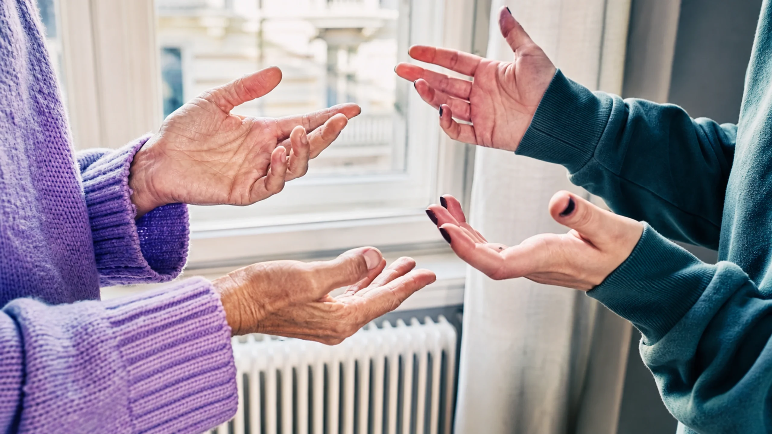 Les mains de deux générations esquissent des gestes lors d'une conversation calme.